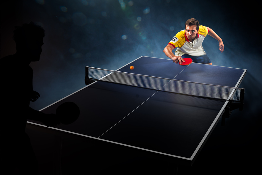 young sports man tennis player playing on black background with lights